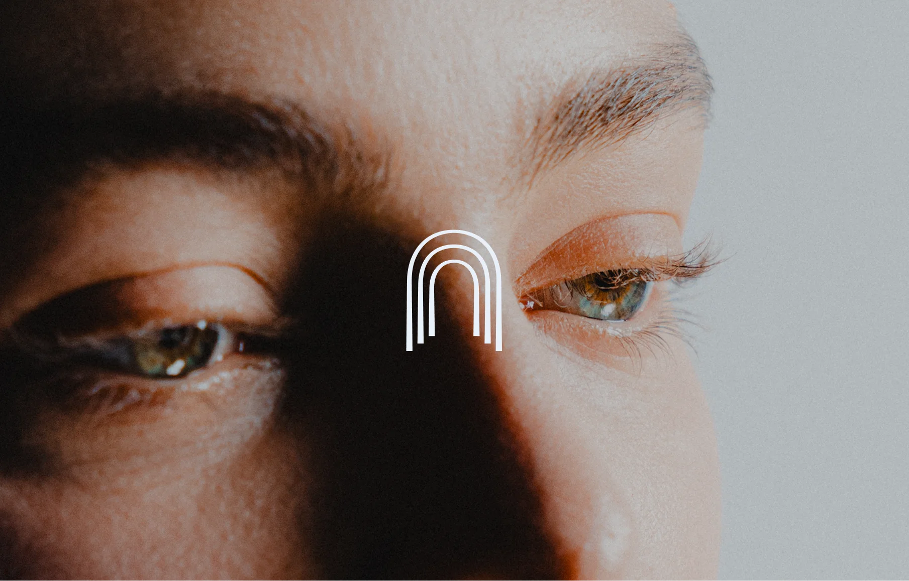 Close-up portrait focused on a woman’s eyes with the white Blue Door Med arch monogram centered over the image